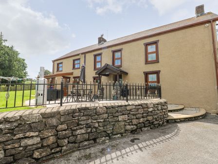 A stone wall and metal fence surrounding a patio area with outdoor furniture beside a two-story house at Pant Teg Farm in Carmarthen