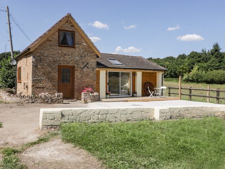 A stone and wood house with a wooden door and sliding glass door a small table and chairs on the patio and a grassy area outside at Steel Works Farm in Gorsley