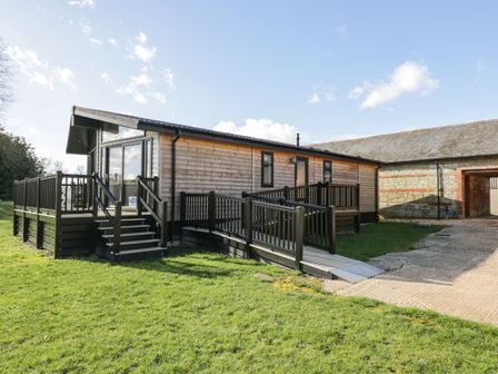 A wooden lodge with a deck and ramp on a grassy area at Manor Farm Lodge in Bowerchalke