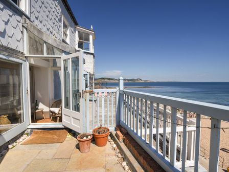 A balcony with potted plants and an open door leading inside overlooking the sea at Bell Cliff House in Lyme Regis