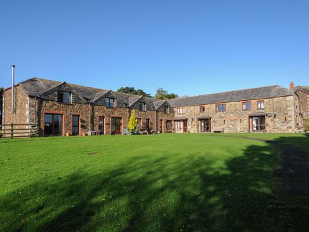 A large stone building with multiple windows and a grassy lawn in front at The Snug in St Minver