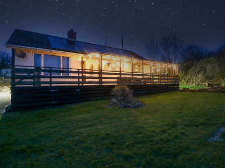 A house with a porch lit up at night with a starry sky in the background at Petlyns Patch in Gwalchmai near Llangefni
