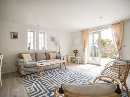 A living room with a sofa cushions coffee table armchairs rug and glass doors at 1 Buckfields in Lyme Regis
