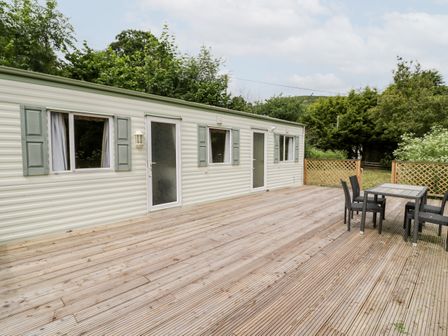 A wooden deck with a black table and four chairs outside a caravan with green shutters and two doors at Grange Caravan in Llangollen
