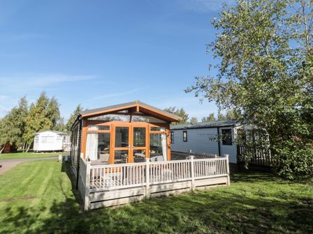 A mobile home with wooden framed glass doors and a fenced porch on a grassy plot at Pinecone Lodge No 9 Felmoor Park near Felton