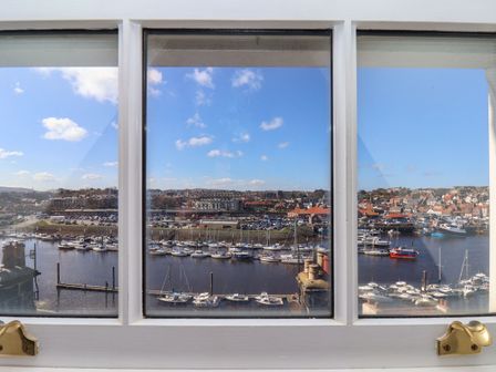 A view of a marina with boats and buildings seen through a window at Navigators Rest in Whitby