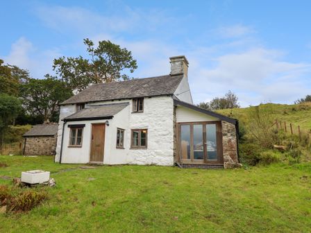 A stone and white plaster cottage with wooden doors and windows in a grassy area at Ty Newydd Uchaf in Brithdir near Dolgellau