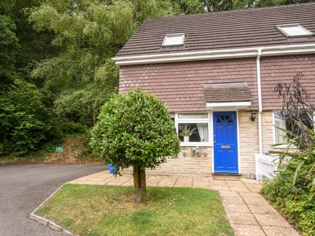 The exterior of a house with a blue front door a small tree on a grassy lawn and a paved pathway at 52 Fernhill Heights Charmouth