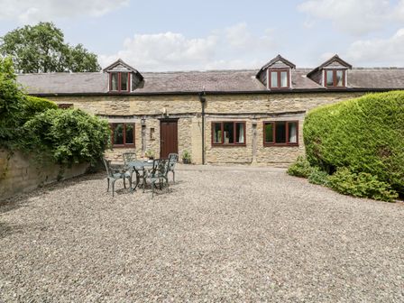 A stone cottage with four windows and a door with a gravel patio and outdoor table and chairs surrounded by shrubs at Redstart Cottage in Kingsland