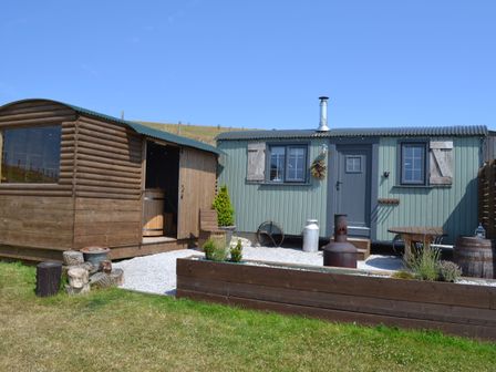 An outdoor area with two small buildings a wooden cabin and a green metal hut with a chimney and garden beds at Heather Hut at Copy House Hideaway in Earby