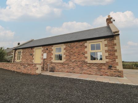 A brick cottage with two windows and a door on a paved area at Whinny Cottage in Embleton