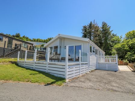 A white single-story house with glass and white fencing on a paved driveway at Ystwyth 36 in Borth