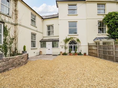 A gravel driveway in front of a white building with windows and a wooden fence at White Roses in Whitchurch near Monmouth
