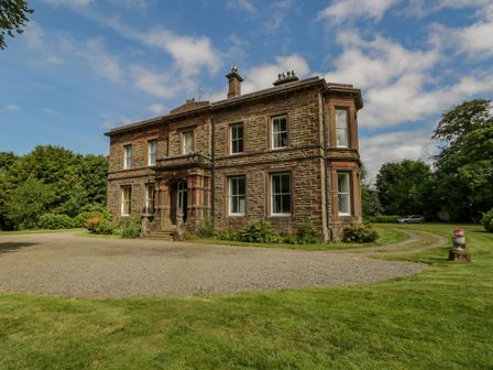 A large brick house with a gravel driveway and grass lawn surrounded by trees at The Residence in Cleator