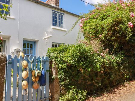A white cottage with blue wooden gate decorated with buoys and flowers at Gwynn Cottage in St Mabyn