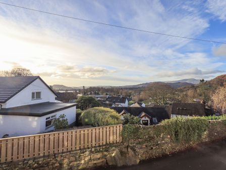 A view of houses trees hills and sky from behind a wooden fence and stone wall at Violet Cottage in Ambleside