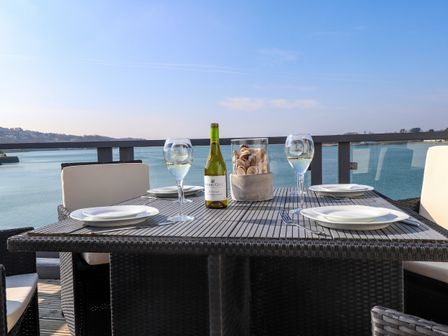 An outdoor dining table set with plates wine glasses a bottle and a seashell centerpiece overlooking water at White Sails in Y Felinheli