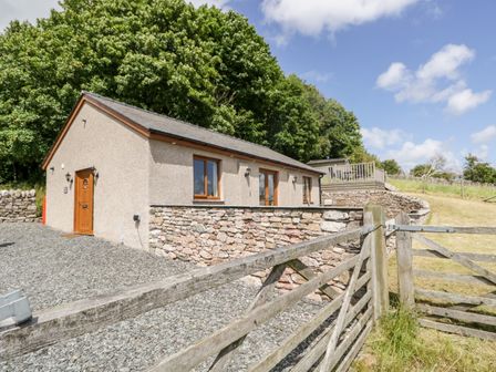 A single-story house with stone and stucco walls surrounded by trees and a wooden gate at Little Barn in Grange-Over-Sands near Cartmel