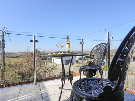 A balcony with black metal chairs and a round table with a bottle and two glasses overlooking a rural area at Escape To The Chapel Anglesey Bryngwran near Rhosneigr