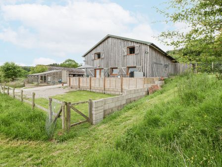 A wooden barn style building with a fenced grassy yard and a gravel driveway at Top Lodge in Llanvair-Discoed near Penhow