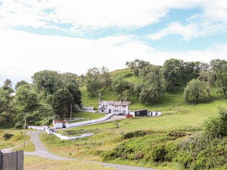 A countryside house with white walls surrounded by green hills and trees at Pyllau Farm in Llandudno