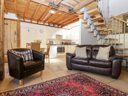 A living room with brown leather sofa and armchair near a wooden dining table and white kitchen at Nympy Cottage in Nympsfield near Nailsworth
