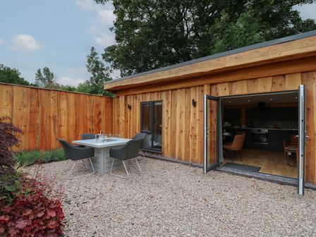 An outdoor patio area with a table and four chairs next to a wooden building with open double doors at Celyn in Llangadfan