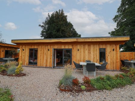A wooden cabin with glass doors and outdoor tables and chairs on a gravel patio at Fioled in Llangadfan