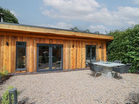 An outdoor area with gravel flooring a wooden building with large windows and a door and a table with four chairs at Pansi in Llangadfan
