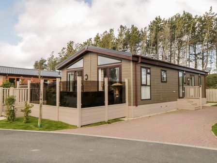 A modern single-story cabin with a fenced patio and paved driveway surrounded by trees at Rockpool Retreat in Runswick Bay near Hinderwell