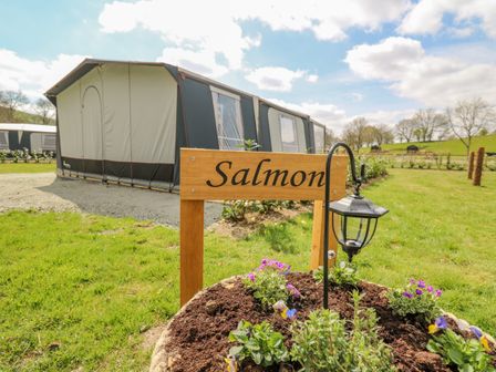 A camping tent with a wooden sign saying Salmon and a flower bed with a lamp at The Salmon in Nantmel near Rhayader