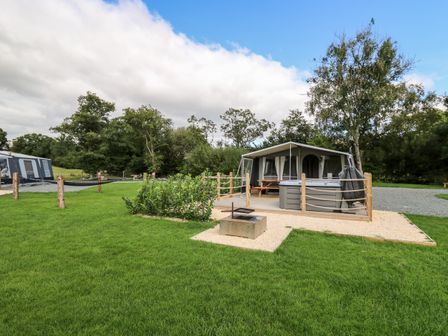 A grassy outdoor area with a tent and a wooden deck with a hot tub and picnic table at The Otter in Nantmel near Rhayader