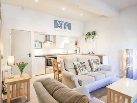 A living room with sofas and cushions next to a kitchen with wooden furniture and plants at Cringol Cottage in Ambleside