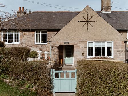 A stone cottage with a compass design on the gable and a light blue gate at the entrance at Compass Cottage in Wooler