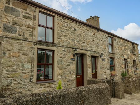 A stone exterior of two connected houses with wooden framed windows and front doors at Dwyros in Morfa Nefyn