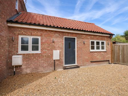 Brick building with two white framed windows and a dark door on a gravel ground at Crab Cottage in Wells-Next-The-Sea