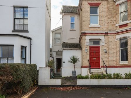 The exterior of two attached houses with a red front door and potted plants at Mimosa in Dawlish