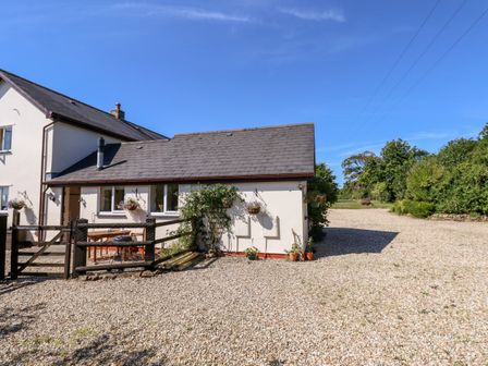 A small house with a gravel driveway and wooden gate surrounded by trees and bushes at Little Rowan at Rowan Park Farm in Ashwater