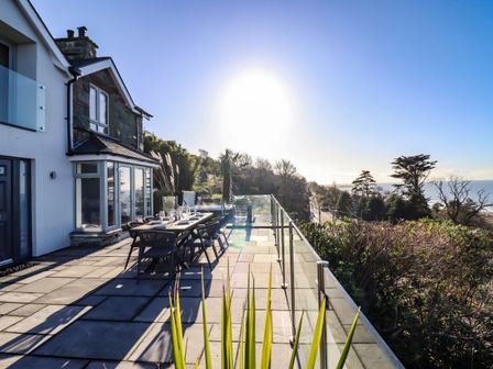 An outdoor patio with a dining table and chairs next to a house surrounded by trees and overlooking the sea at Aelfor in Harlech