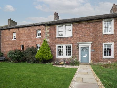A brick house with a blue door and white framed windows with a garden path leading to the entrance at The Hollies in Thurstonfield near Carlisle