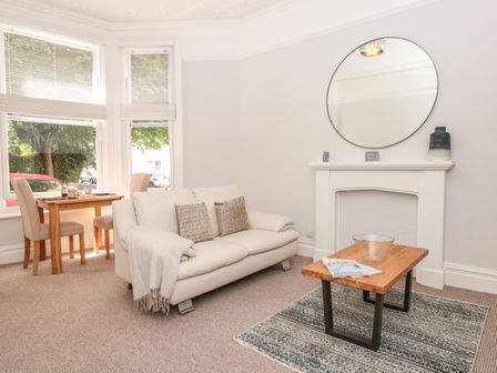 A living room with a white sofa coffee table by a fireplace and a dining table with chairs by the window at Flat 1 Byfield in Torquay