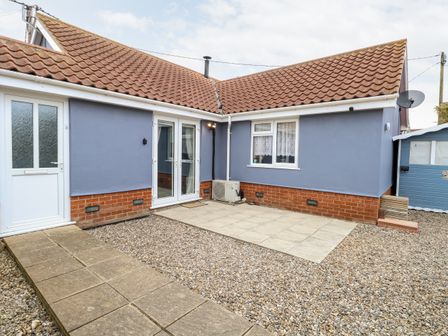 A courtyard area outside a blue bungalow with a tiled roof and gravel ground at Kingfisher Lodge in Hemsby