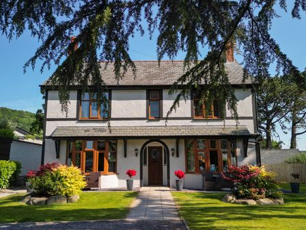 A two-story house with wooden framed windows and a front door with plants in pots on either side at Y Gorlan in Rowen near Conwy