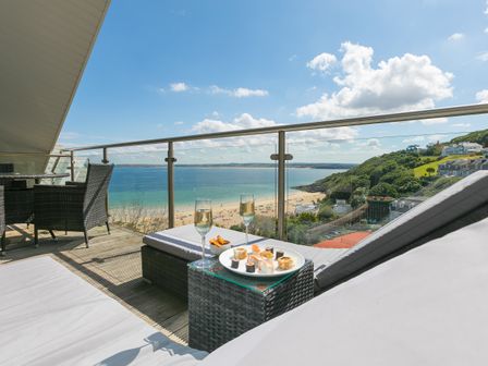 A balcony with lounge chairs a table with sushi and drinks overlooking a beach and sea at Porthminster Penthouse in St Ives