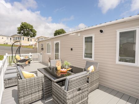 An outdoor deck with a wicker dining table and chairs and a hanging chair at Moondunes - Pwllheli in Chwilog