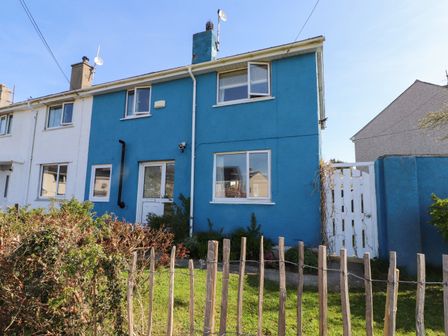 A blue end terrace house with white windows and doors a wooden fence and green grass at 11 Penygroes in Llanddeusant