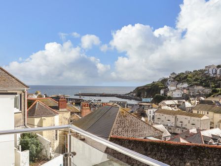A coastal town view with rooftops chimneys a harbor sea and hillside houses at Chy An Mor in Mevagissey