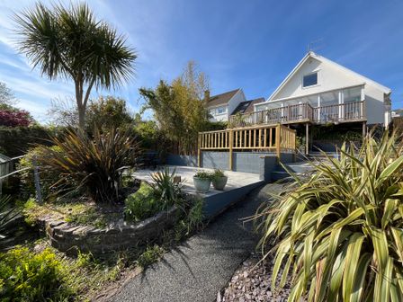 A garden with plants a wooden deck and a house in the background at Old Orchard Saundersfoot