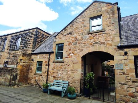 A stone building with an arched entrance and a blue bench outside at Dodds Nook in Alnwick