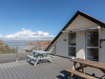 A rooftop terrace with picnic benches and a glass railing overlooking the sea at Goody in Hope Cove